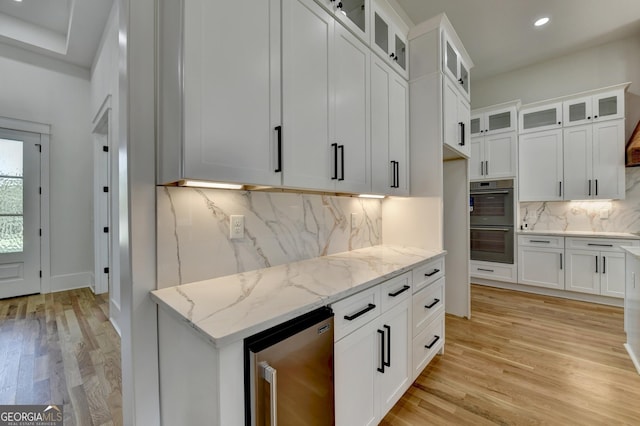 kitchen with white cabinetry, double oven, light stone counters, and light hardwood / wood-style flooring