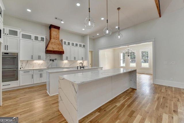 kitchen with a kitchen island, double oven, custom exhaust hood, and white cabinets