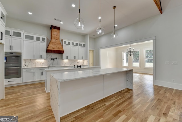 kitchen with custom exhaust hood, hanging light fixtures, stainless steel double oven, and white cabinets