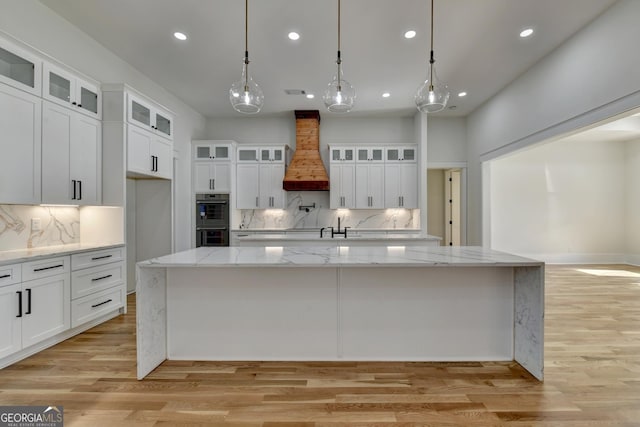 kitchen with a spacious island, hanging light fixtures, custom exhaust hood, and white cabinets