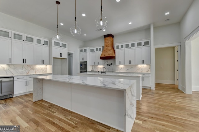 kitchen with premium range hood, hanging light fixtures, white cabinets, a center island with sink, and stainless steel dishwasher