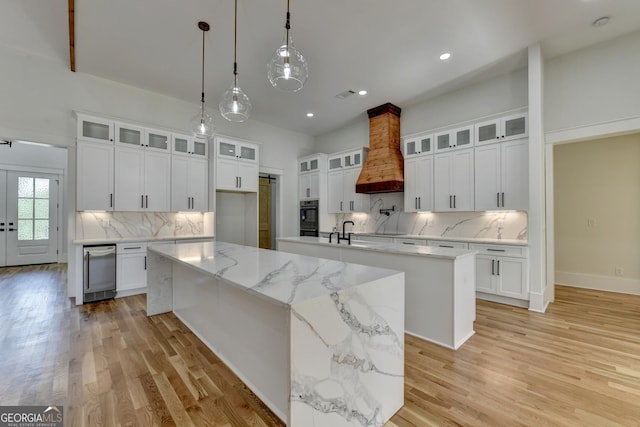 kitchen with white cabinets, custom exhaust hood, and a large island with sink