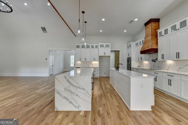 kitchen featuring pendant lighting, white cabinetry, sink, a large island with sink, and light hardwood / wood-style flooring