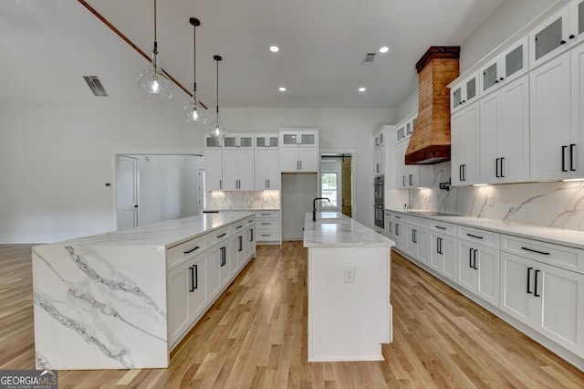 kitchen featuring pendant lighting, a center island with sink, white cabinets, and light stone counters