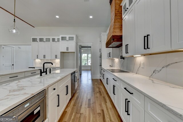 kitchen with white cabinetry, hanging light fixtures, light stone counters, and sink