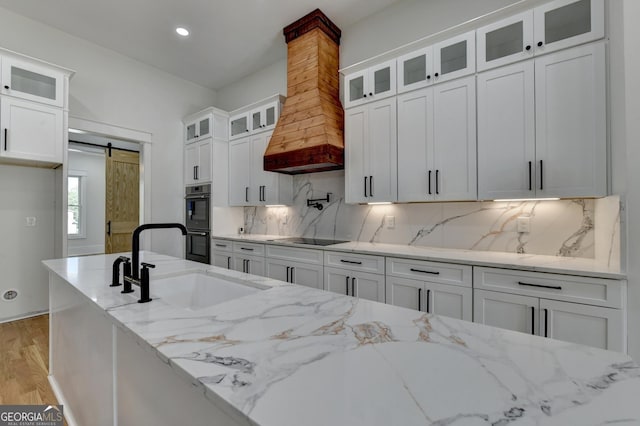 kitchen with sink, light stone countertops, a barn door, and white cabinets