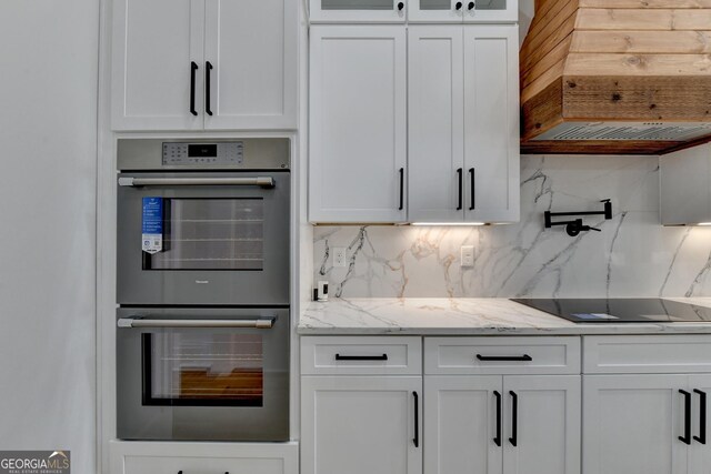 kitchen with double oven, backsplash, light stone counters, white cabinets, and black electric cooktop