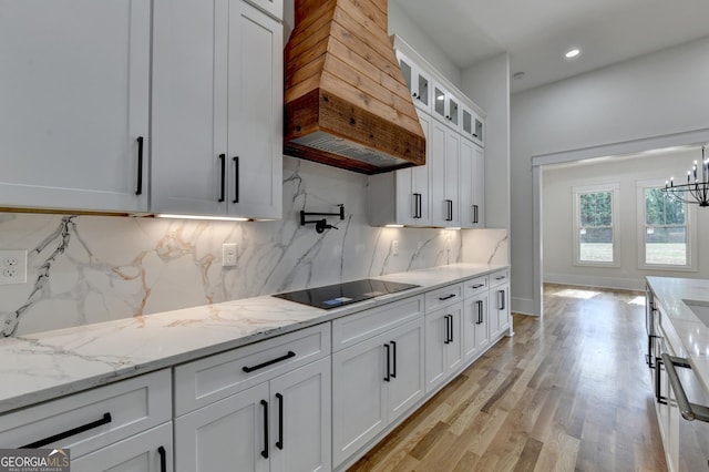 kitchen with white cabinetry, custom exhaust hood, black electric cooktop, light stone counters, and light wood-type flooring