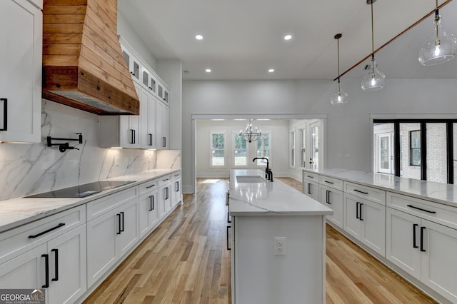 kitchen featuring sink, white cabinetry, hanging light fixtures, black electric stovetop, and a kitchen island with sink