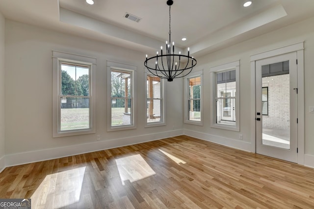 unfurnished dining area with a raised ceiling, a notable chandelier, and light hardwood / wood-style floors