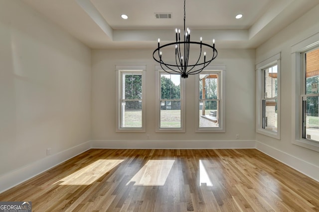 unfurnished dining area with an inviting chandelier, a raised ceiling, and light wood-type flooring