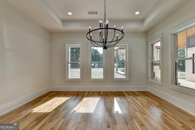 unfurnished dining area featuring a tray ceiling, a wealth of natural light, and light wood-type flooring