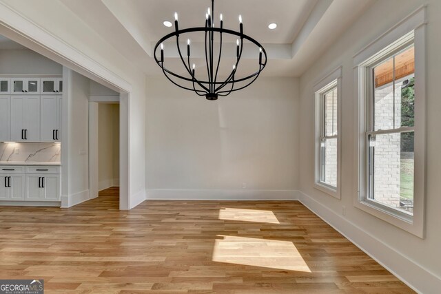 unfurnished dining area featuring a raised ceiling, plenty of natural light, an inviting chandelier, and light wood-type flooring