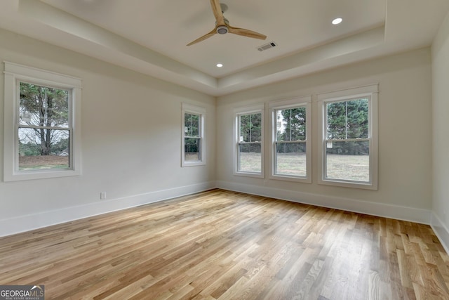 spare room featuring a raised ceiling, ceiling fan, and light hardwood / wood-style floors