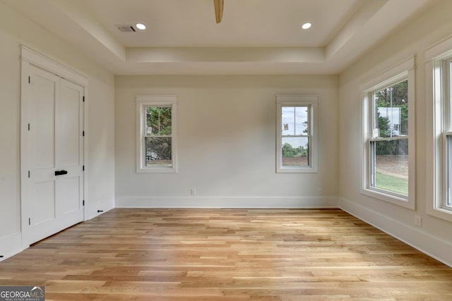 empty room with a tray ceiling and light hardwood / wood-style flooring