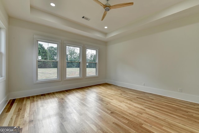 spare room featuring a raised ceiling, ceiling fan, and light hardwood / wood-style floors