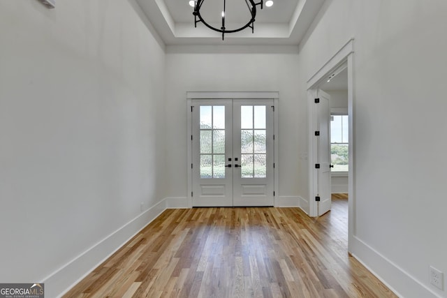 doorway to outside featuring a raised ceiling, a chandelier, light wood-type flooring, and french doors