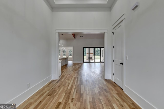 corridor with an inviting chandelier, a towering ceiling, and light hardwood / wood-style flooring