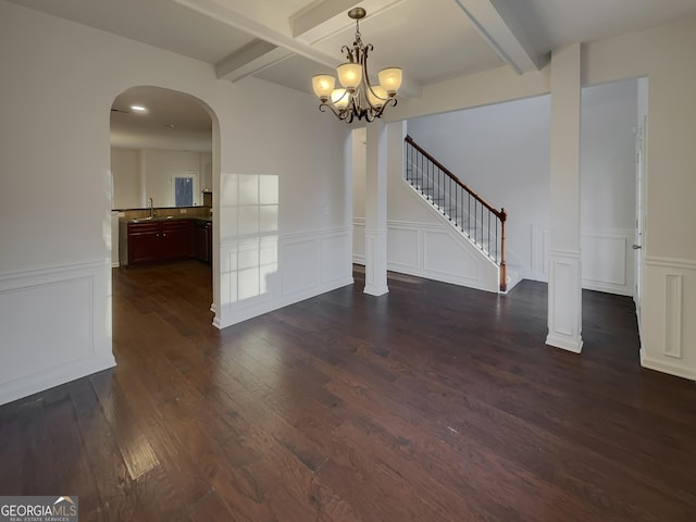 unfurnished dining area with sink, an inviting chandelier, beam ceiling, decorative columns, and dark hardwood / wood-style floors