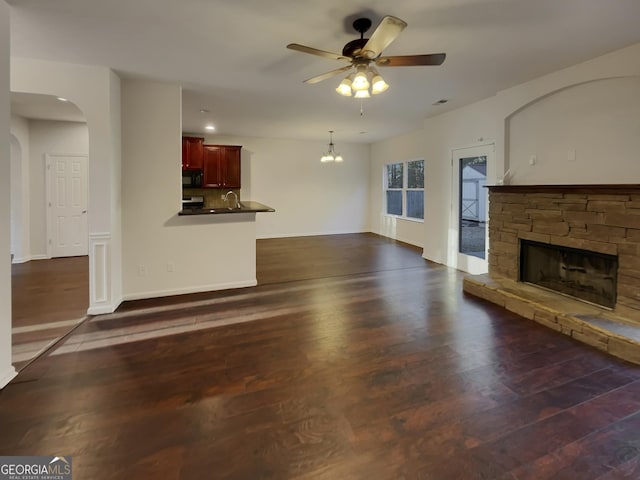 unfurnished living room featuring sink, a fireplace, dark hardwood / wood-style flooring, and ceiling fan with notable chandelier