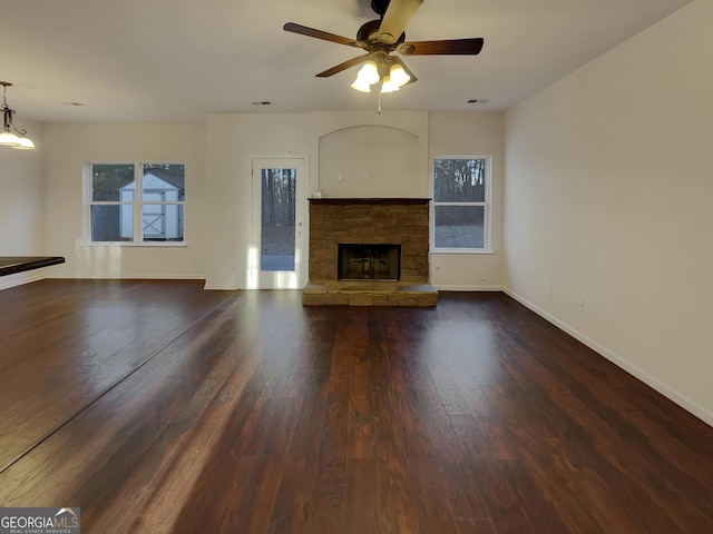 unfurnished living room with ceiling fan, dark hardwood / wood-style floors, and a stone fireplace