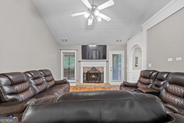 living room featuring ceiling fan, a stone fireplace, wood-type flooring, and a textured ceiling