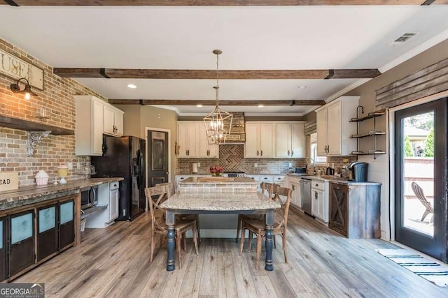 kitchen with light stone counters, a center island, hanging light fixtures, light wood-type flooring, and beamed ceiling