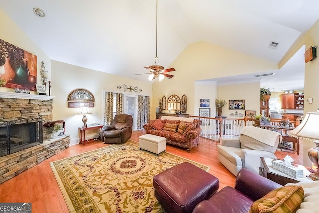 living room featuring a stone fireplace, high vaulted ceiling, ceiling fan, and light wood-type flooring