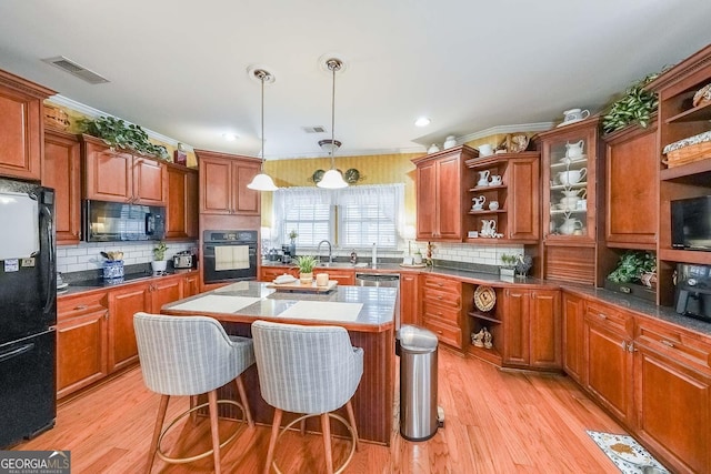 kitchen with a breakfast bar, decorative light fixtures, a center island, black appliances, and light hardwood / wood-style flooring