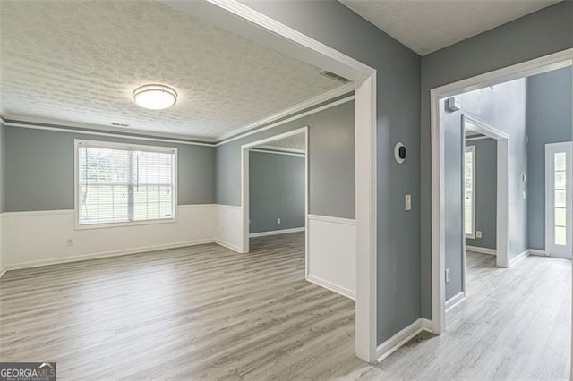 spare room with crown molding, light hardwood / wood-style flooring, and a textured ceiling