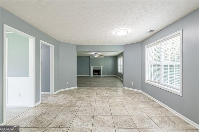 unfurnished living room featuring ceiling fan, light tile patterned floors, and a textured ceiling