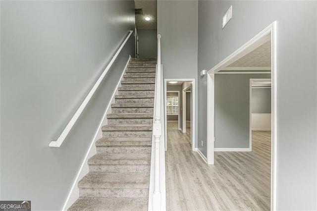 staircase with a towering ceiling, wood-type flooring, and ornamental molding