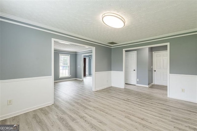 spare room featuring ornamental molding, a textured ceiling, and light wood-type flooring