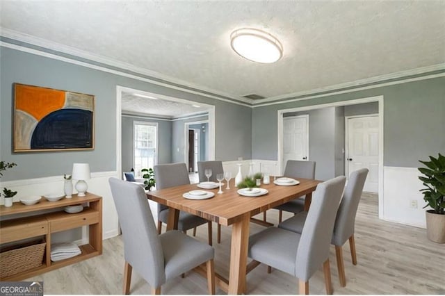 dining space featuring crown molding, a textured ceiling, and light hardwood / wood-style flooring