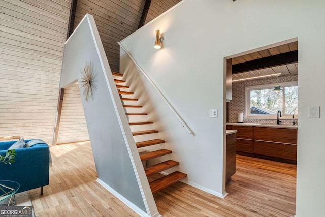 stairway with hardwood / wood-style floors, high vaulted ceiling, sink, wooden ceiling, and beam ceiling