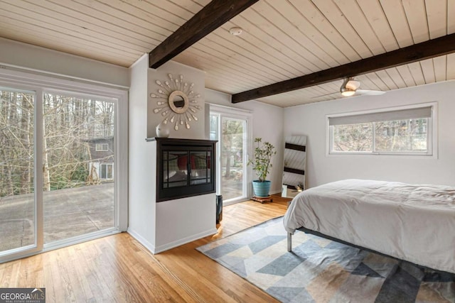 bedroom with a multi sided fireplace, light hardwood / wood-style flooring, multiple windows, and access to outside