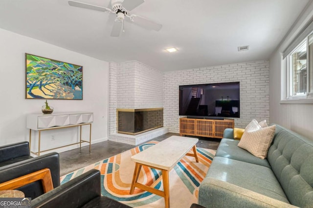 living room featuring ceiling fan, brick wall, a brick fireplace, and concrete floors