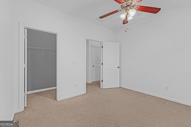 unfurnished bedroom with light carpet, a walk in closet, a closet, and ceiling fan