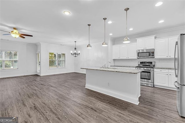 kitchen with white cabinetry, hanging light fixtures, appliances with stainless steel finishes, light stone countertops, and a kitchen island with sink