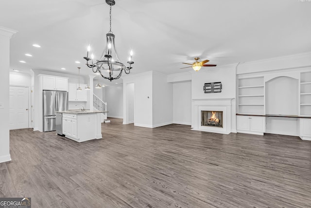 kitchen with sink, decorative light fixtures, stainless steel refrigerator, a kitchen island with sink, and white cabinets