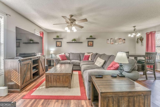 living room featuring hardwood / wood-style floors, ceiling fan with notable chandelier, and a textured ceiling