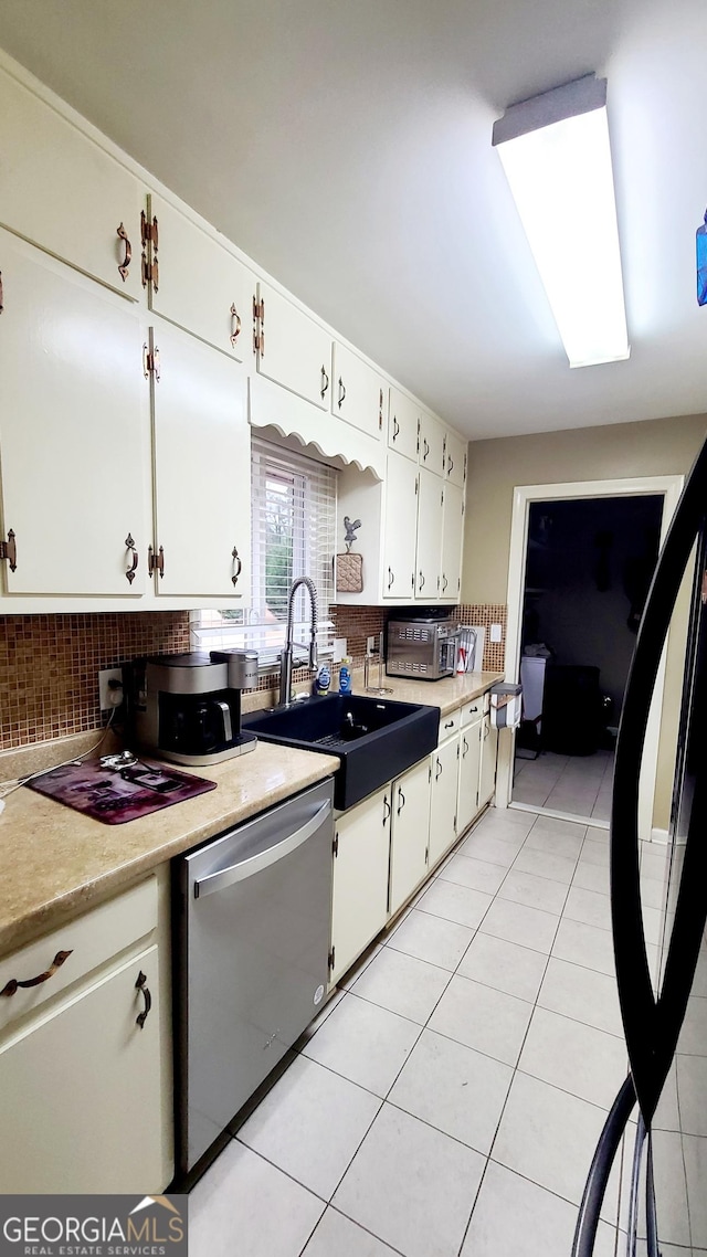 kitchen with tasteful backsplash, sink, white cabinets, stainless steel dishwasher, and light tile patterned floors