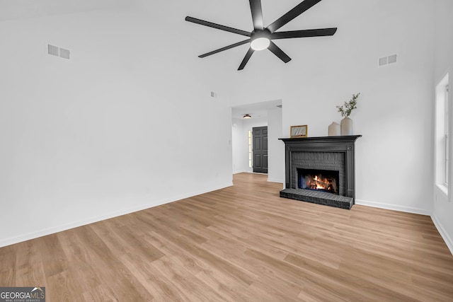 unfurnished living room with a brick fireplace, ceiling fan, a high ceiling, and light wood-type flooring