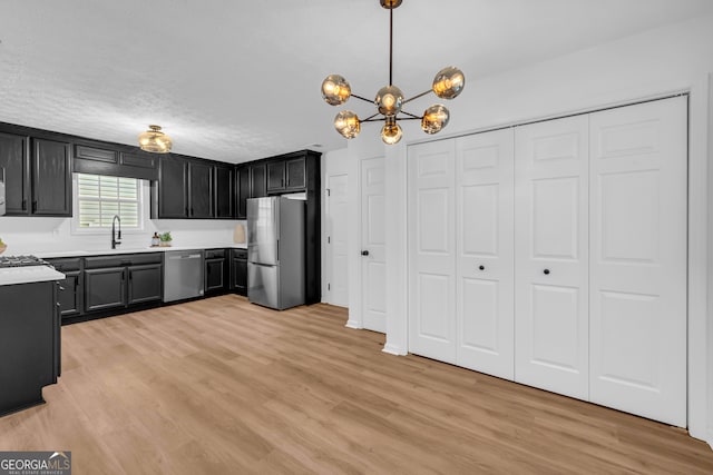 kitchen with sink, an inviting chandelier, light hardwood / wood-style flooring, appliances with stainless steel finishes, and pendant lighting