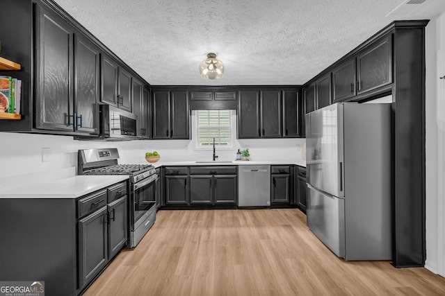 kitchen with appliances with stainless steel finishes, sink, a textured ceiling, and light hardwood / wood-style floors