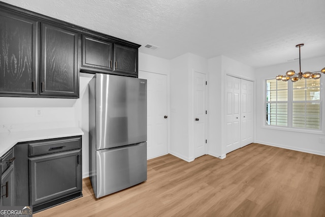 kitchen featuring a textured ceiling, pendant lighting, stainless steel fridge, and light wood-type flooring