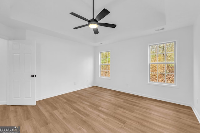 spare room with ceiling fan, a raised ceiling, and light hardwood / wood-style flooring