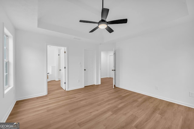 unfurnished bedroom featuring a raised ceiling, ceiling fan, and light hardwood / wood-style floors