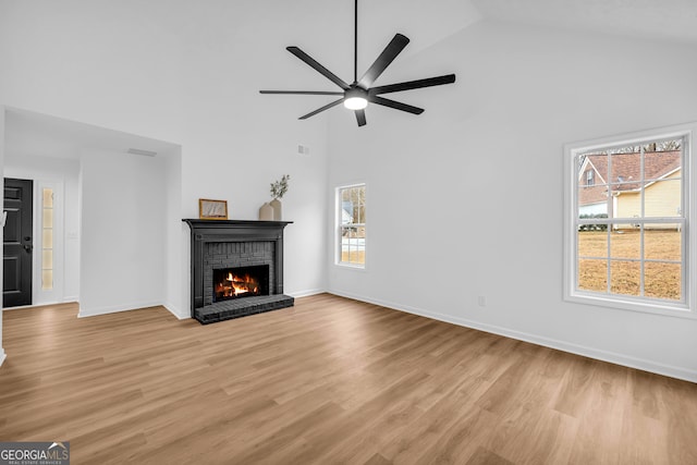 unfurnished living room with a brick fireplace, light hardwood / wood-style floors, high vaulted ceiling, and ceiling fan