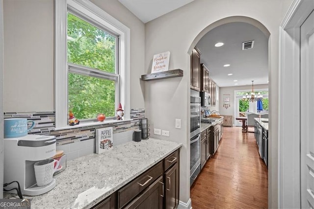 kitchen featuring hardwood / wood-style floors, decorative light fixtures, tasteful backsplash, dark brown cabinetry, and light stone countertops